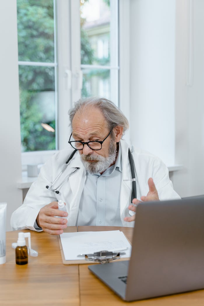 portfolio-01 Elderly doctor explaining medication during an online consultation in a well-lit office setting.
